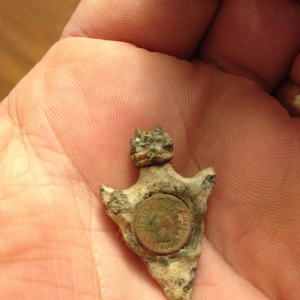 Found this "arrowhead" with an "indianhead penny" embedded in it in an old park.  Penny is about 1/2 size so not real.  Any ideas on what this came fr