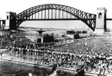 New Yorkers cool off in the Astoria public pool with the Hell Gate railroad bridge looming in...webp
