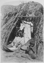Paiute_woman_grinding_seeds_in_doorway_of_thatched_hut,_small_boy_in_foreground,_1872_-_NARA_...webp